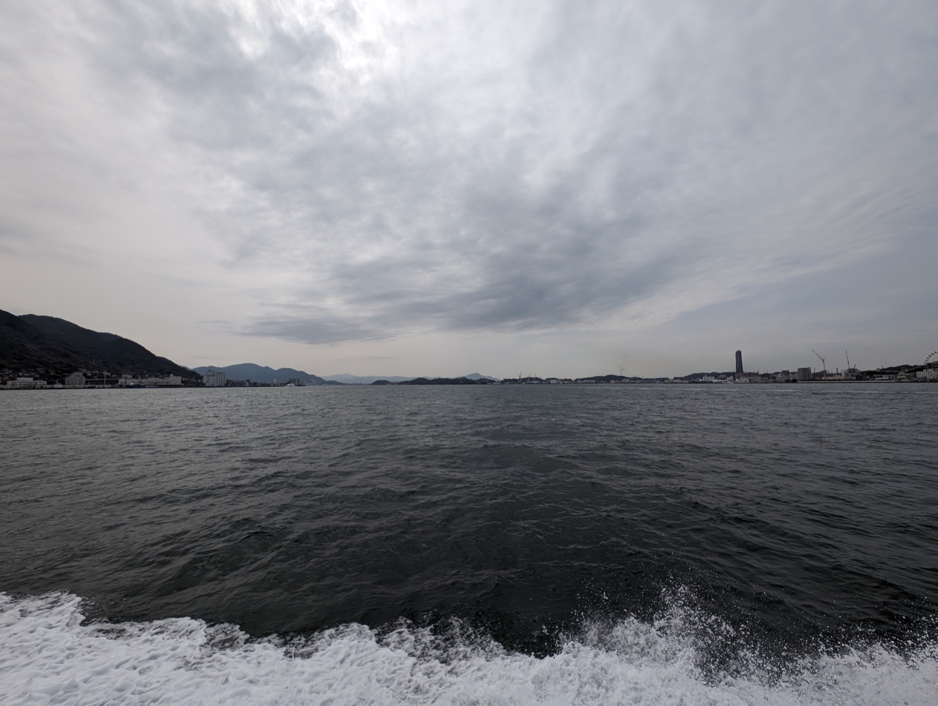 White spray of the boat's wash contrasts with an almost black sea with mountains and silver clouds in the far distance